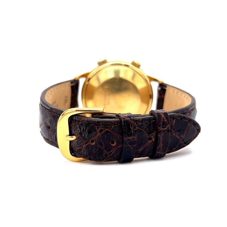 May include: A gold-tone wristwatch with a brown leather band. The watch has a round face and a chronograph function.