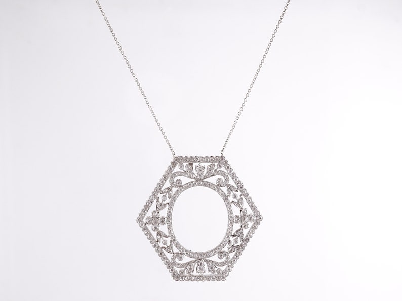 May include: A silver necklace with a hexagonal pendant featuring a delicate, intricate design of small diamonds. The pendant has a circular opening in the center.