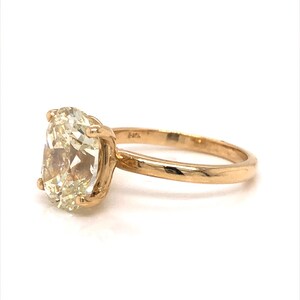 Pode incluir: Um anel de ouro com uma grande gema oval de cor amarelo claro. O anel &eacute; definido em um estilo simples e cl&aacute;ssico.