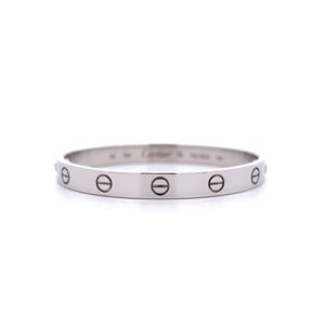 May include: A silver-toned metal bangle bracelet featuring a smooth, polished surface. The band is decorated with a repeating pattern of engraved screw head motifs around the exterior. The word Cartier is engraved on the inner surface of the band.