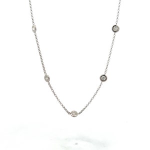 Puede incluir: Un delicado collar de plata con cinco diamantes redondos engastados en biseles, espaciados a lo largo de una fina cadena. Los diamantes brillan con la luz, creando un diseño minimalista y elegante. El collar se muestra sobre un fondo blanco.