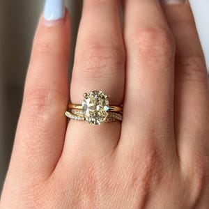 Pode incluir: Um anel de noivado de ouro com um grande diamante oval. O anel &eacute; usado no dedo anelar de uma m&atilde;o com esmalte de unha azul claro.