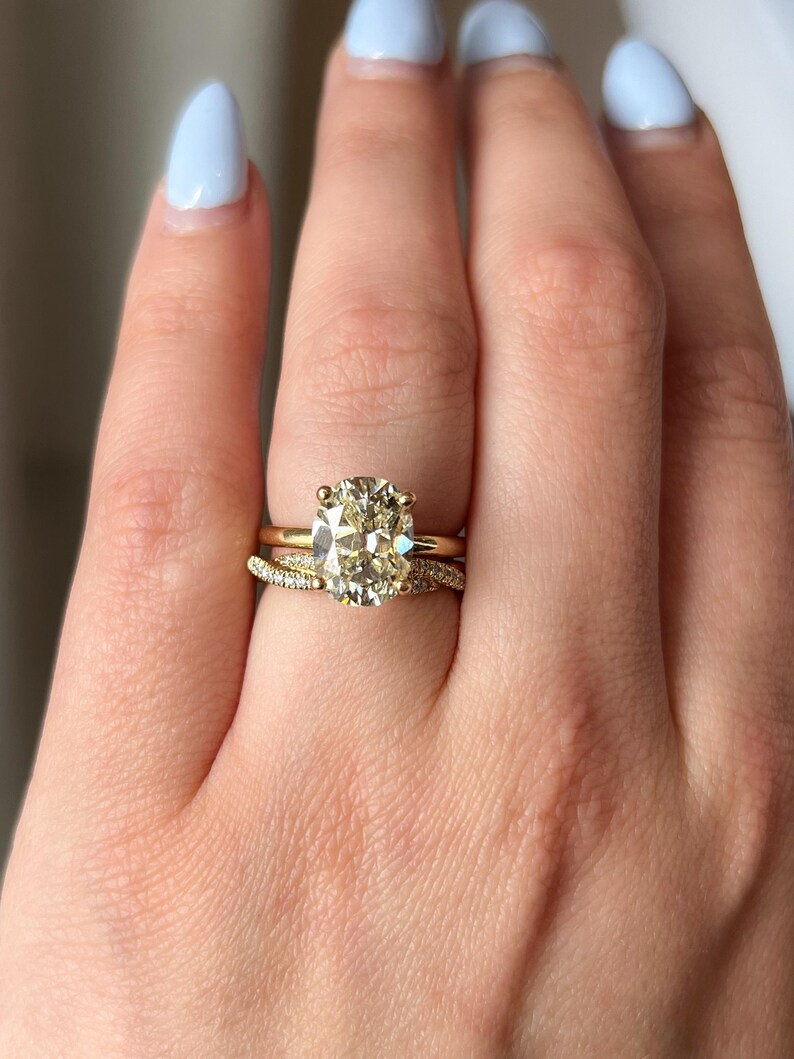 Pode incluir: Um anel de noivado de ouro com um grande diamante oval. O anel &eacute; usado no dedo anelar de uma m&atilde;o com esmalte de unha azul claro.