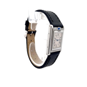 May include: Side view of a Cartier Tank watch with a black leather strap. The watch has a rectangular silver case and a white dial with black Roman numerals. The watch features a sapphire crystal and a quartz movement.  The strap has a subtle textured pattern. The watch is elegant and classic in design.