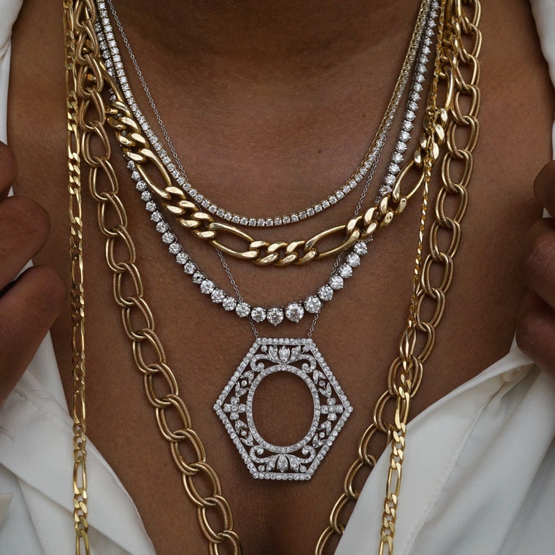 May include: A layered gold chain necklace with a large, hexagonal pendant set with sparkling diamonds. The pendant features a circular design in the center.