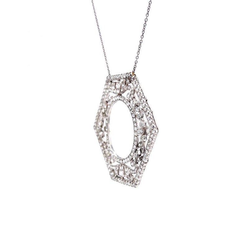 May include: A silver necklace with a hexagonal pendant encrusted with small, clear gemstones. The pendant is open in the center, creating a circular shape.