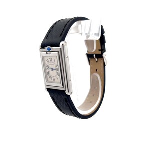 May include: A Cartier Tank watch with a rectangular silver face, black Roman numeral hour markers, and blue hands. The watch has a black fabric band and a stainless steel case. The watch is shown in profile view, with the face angled slightly toward the viewer. The watch's brand name is visible on the face. The watch is a classic and elegant timepiece, suitable for both men and women.