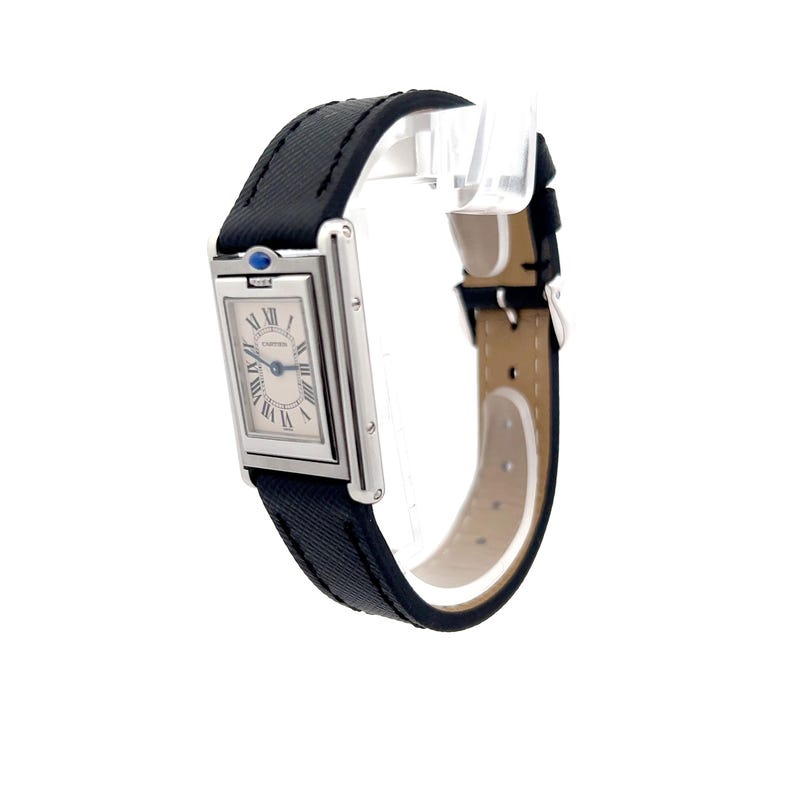 May include: A Cartier Tank watch with a rectangular silver face, black Roman numeral hour markers, and blue hands. The watch has a black fabric band and a stainless steel case. The watch is shown in profile view, with the face angled slightly toward the viewer. The watch's brand name is visible on the face. The watch is a classic and elegant timepiece, suitable for both men and women.