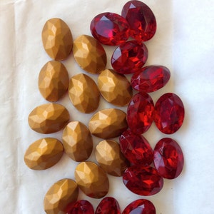 May include: A collection of red and gold oval-shaped glass gems. The gems are arranged in a random pattern on a white surface.