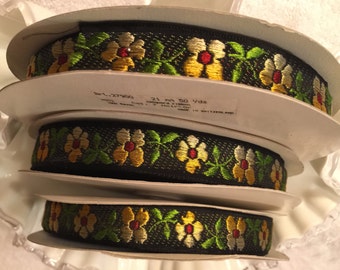 Puede incluir: Tres carretes de cinta negra con un patrón floral en amarillo, verde, rojo y blanco. La cinta tiene 21 mm de ancho y 50 yardas de largo. La etiqueta dice "Part. 27900 21 mm 50 Yds."