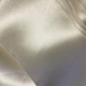 May include: A close-up of a white satin ribbon with a smooth, silky texture. The ribbon is folded in a way that creates a diagonal pattern.