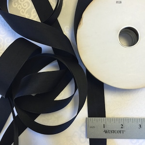 May include: A spool of black nylon ribbon with a white label that reads "50 YARDS NYLON". The ribbon is 1 inch wide and is lying on a white surface with a ruler.