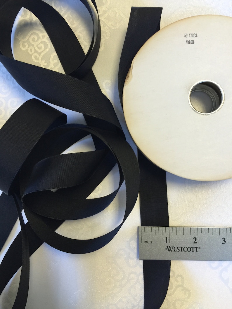 May include: A spool of black nylon ribbon with a white label that reads "50 YARDS NYLON". The ribbon is 1 inch wide and is lying on a white surface with a ruler.