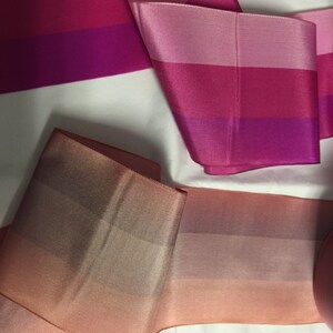 Puede incluir: Tres tipos diferentes de cinta con un patr&oacute;n a rayas. La primera cinta es rosa, roja y morada. La segunda cinta es rosa, roja y morada. La tercera cinta es un degradado de melocot&oacute;n, rosa y marr&oacute;n.