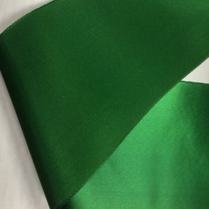 Pu&ograve; includere: Primo piano di un nastro verde con finitura satinata. Il nastro &egrave; piegato a met&agrave;, mostrando entrambi i lati del tessuto.