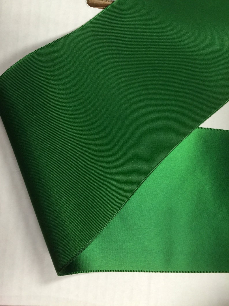 Pu&ograve; includere: Primo piano di un nastro verde con finitura satinata. Il nastro &egrave; piegato a met&agrave;, mostrando entrambi i lati del tessuto.
