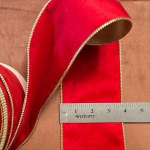Könnte beinhalten: Rotes Samtband mit goldener Einfassung. Das Band ist 5 cm breit und wird um ein Lineal gewickelt gezeigt.