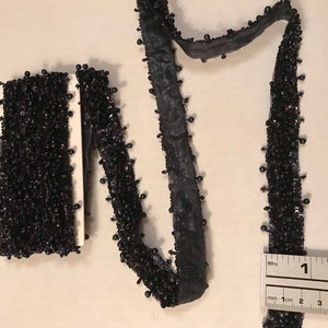 Könnte beinhalten: Schwarzer Perlenbesatz mit schwarzem Stoffrücken. Der Besatz ist etwa 5 cm lang und wird neben einem Lineal gezeigt.