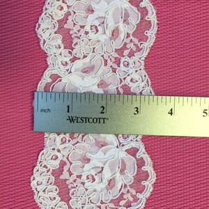 Op de afbeelding: Witte kant met een bloemenpatroon. De kant is ongeveer 5 cm breed.