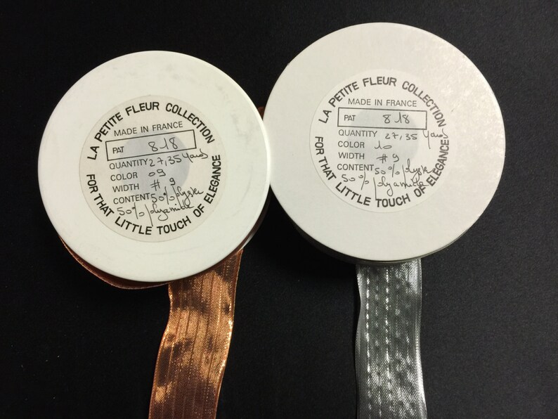 K&ouml;nnte beinhalten: Zwei wei&szlig;e Garnrollen mit Etiketten, auf denen "La Petite Fleur Collection" steht und Details wie "Made in France", "Pat 818", "Menge 2 7/35 Yards", "Farbe #9", "Breite #9" und "Inhalt 50% Seide 50% Nylon" angegeben sind.