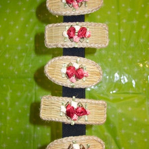 May include: A set of seven hair clips made of woven straw with red and white fabric flowers. The clips are hanging on a black elastic band.