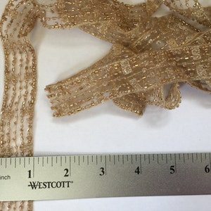 Op de afbeelding: Gouden kralenbies met een metallic glans, 2,5 cm breed. De bies is gemaakt van een delicate mesh stof met kleine, gelijkmatig verdeelde kralen.