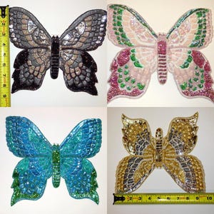 Può includere: Quattro diversi patch di tessuto a forma di farfalla con decorazioni di paillettes. Le farfalle sono in tonalità argento, rosa, blu e oro.