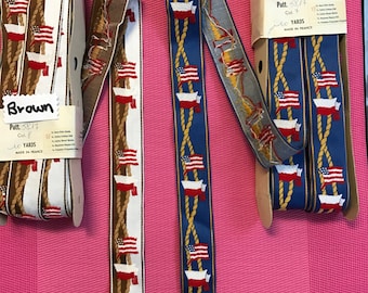May include: Two rolls of fabric trim with a nautical theme. The trim features a white background with a repeating pattern of gold rope, red, white, and blue American flags, and a red and white Polish flag. The trim on the left is brown and the trim on the right is blue. The labels on the trim read "Brown" and "Blue".