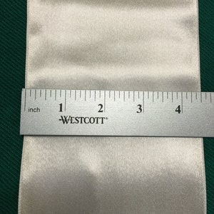 May include: A close-up of a white satin ribbon with a ruler measuring 4 inches in length. The ruler is labeled "WESTCOTT" and has markings for inches.