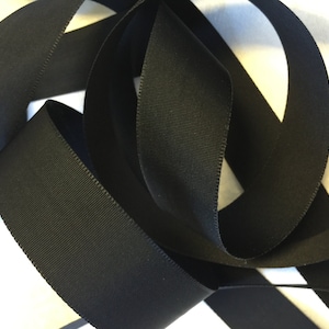 May include: Black grosgrain ribbon, a type of fabric ribbon with a textured, woven surface. The ribbon is folded and arranged in a decorative way.