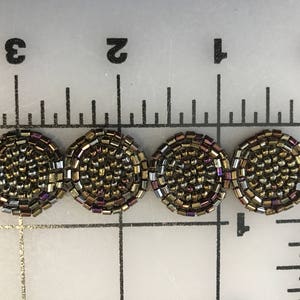 Puede incluir: Primer plano de una fila de cinco piezas redondas de adorno de cuentas. El adorno está hecho de pequeñas cuentas iridiscentes en tonos dorados, marrones y morados. El adorno tiene un diámetro de aproximadamente 2,5 cm.