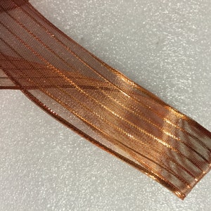 K&ouml;nnte beinhalten: Nahaufnahme eines durchsichtigen Bandes in Kupferfarbe mit einem metallischen Schimmer. Das Band hat eine gewebte Textur und ist in der Mitte gefaltet.