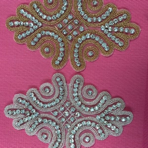 May include: Two decorative embellishments with a floral design. The top embellishment is gold with clear rhinestones. The bottom embellishment is silver with clear rhinestones.