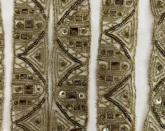 Pode incluir: Trimming de contas douradas com um padrão geométrico. O trimming é feito de um tecido transparente com bordado de fio dourado e lantejoulas.