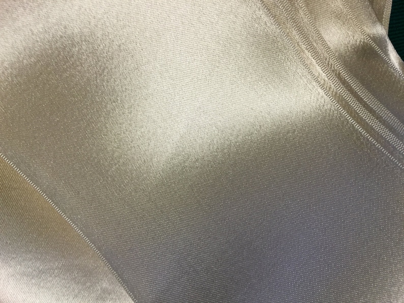 May include: Close-up of a smooth, off-white fabric with a subtle sheen. The fabric has a fine, woven texture and a slight crinkle.