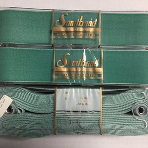 May include: Three spools of teal blue satin ribbon. The ribbon is packaged in clear plastic and labeled "Samband Mit Elastischen", "Festhaftende Seweher fur Flor".