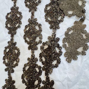 Puede incluir: Primer plano de un ribete de cuentas con un delicado diseño floral. El ribete está hecho de pequeñas cuentas iridiscentes de color marrón oscuro.