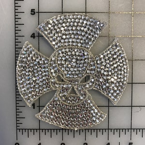 Puede incluir: Un diseño de calavera y huesos cruzados plateado hecho de pedrería. El diseño mide aproximadamente 7,5 cm de ancho.