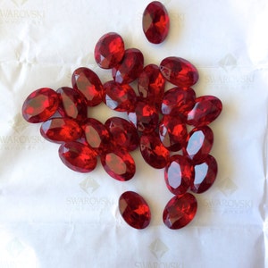 May include: A pile of red oval-shaped rhinestones on a white background.