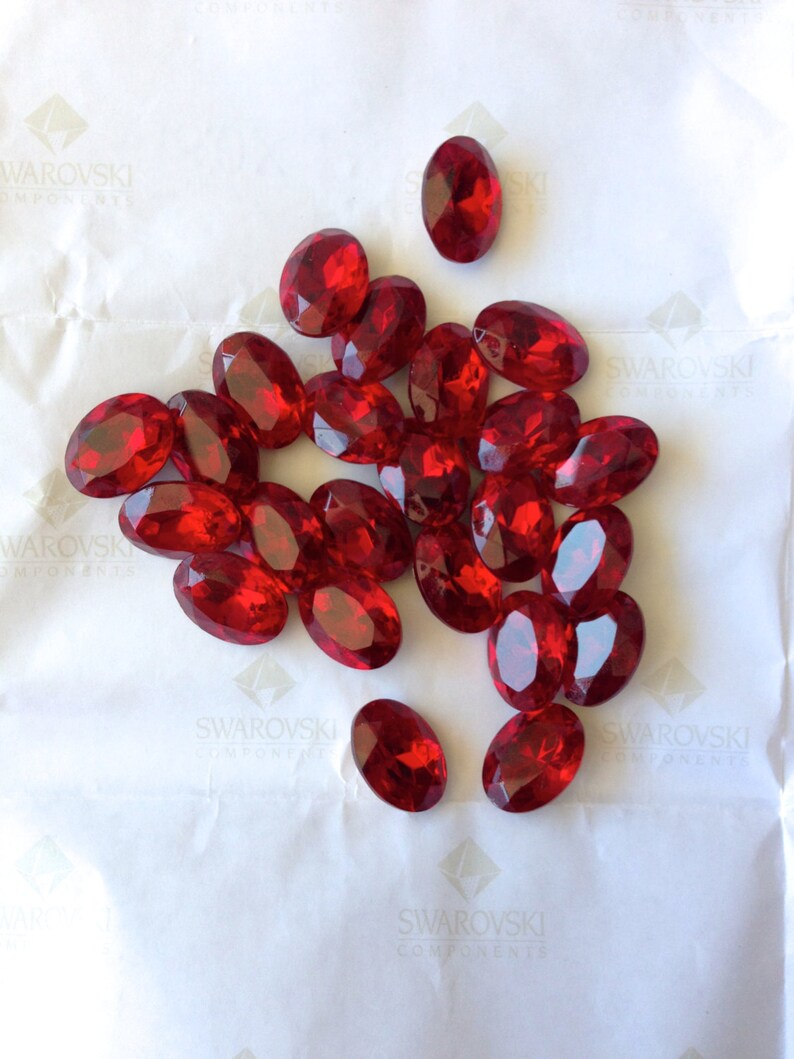 May include: A pile of red oval-shaped rhinestones on a white background.