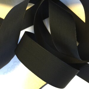May include: Black grosgrain ribbon, a type of fabric ribbon with a textured, woven surface. The ribbon is folded and twisted, showing its width and texture.