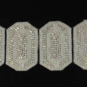 May include: Four silver-colored, octagonal-shaped, beaded patches with a raised design. The patches are arranged in a row.