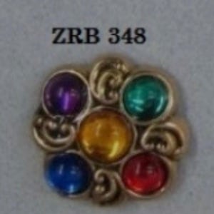 May include: A gold-toned, flower-shaped brooch with seven colorful, round gemstones. The gemstones are purple, green, yellow, blue, and red. The text "ZRB 348" is above the brooch.