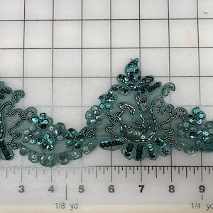 May include: Teal green beaded trim with a floral design. The trim is made of sequins, beads, and a sheer fabric.