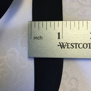 May include: Black ribbon measured with a ruler, showing it is 1 inch wide.