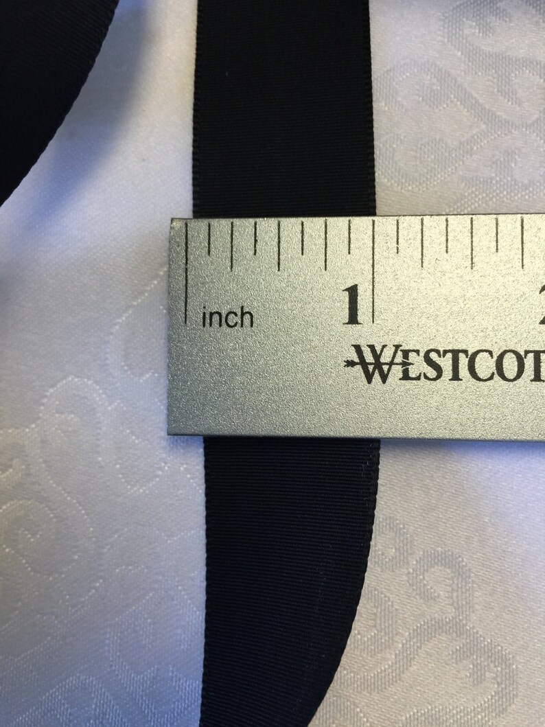 May include: Black ribbon measured with a ruler, showing it is 1 inch wide.