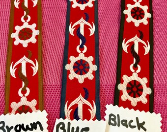May include: Three decorative ribbons with nautical designs. Each ribbon features a red background with white anchors and gear-like shapes. The ribbons are labeled "Brown", "Blue", and "Black".
