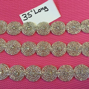 May include: Three rows of silver beaded trim with a central rhinestone in each circle. The trim is 35 inches long.