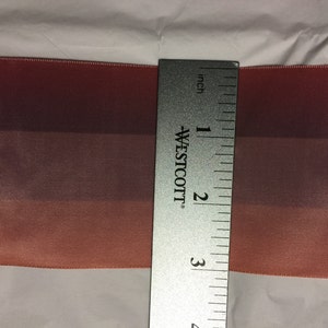 Puede incluir: Primer plano de una cinta degradada de 7,6 cm de ancho con tres tonos de rosa. La cinta se mide con una regla.