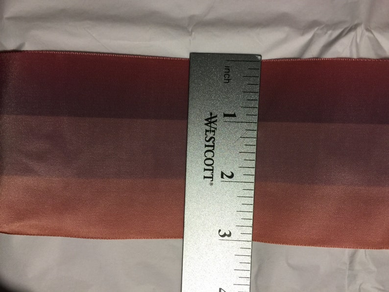 Puede incluir: Primer plano de una cinta degradada de 7,6 cm de ancho con tres tonos de rosa. La cinta se mide con una regla.